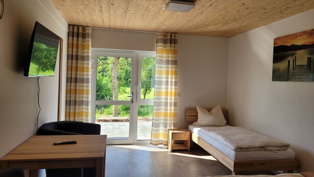 A bedroom with a wooden ceiling, a bed, a desk, a TV, and a window with curtains. - Vacation apartments Meyer, between Nuremberg and Ansbach A6/B14, near Playmobil Fun Park (Heilsbronn)