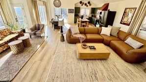 Uma sala de estar espaçosa com um amplo sofá modular marrom, uma mesa de centro e um espaço de jantar com mesa e cadeiras.