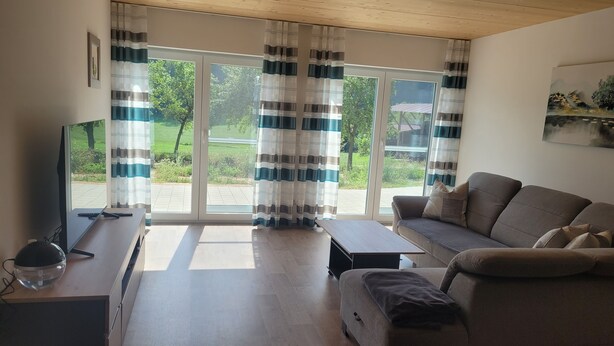 Ein Wohnzimmer mit einer Couch, einem Couchtisch, einem Fernseher und einem Fenster mit Vorhängen.