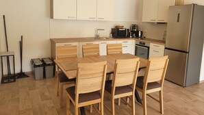 Eine moderne Küche mit weißen Schränken, einem Edelstahlkühlschrank und einem Essbereich mit Holztischen und einer Tischplatte.