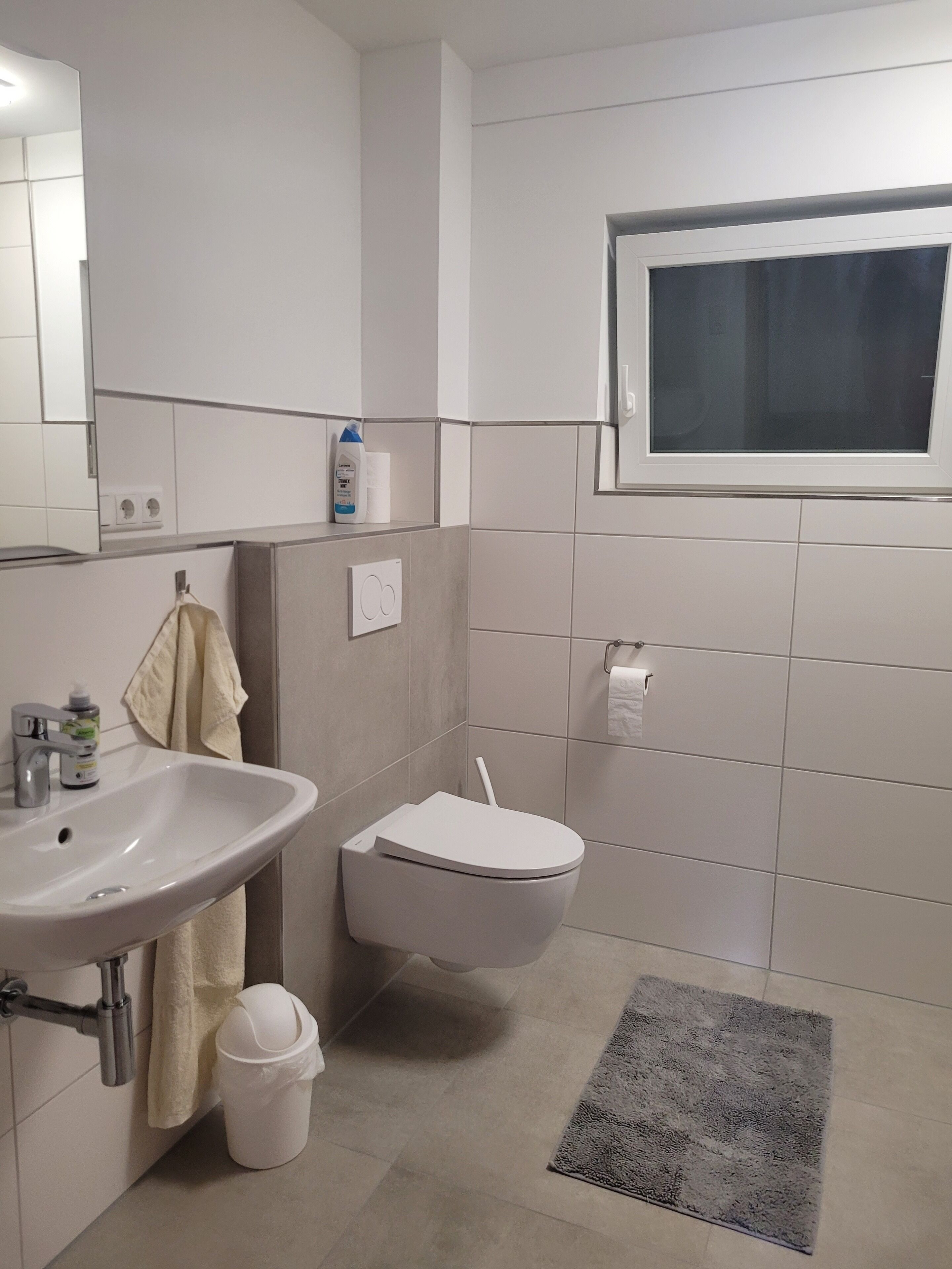A modern bathroom with a white sink, toilet, and a window above the toilet.