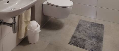 A modern bathroom with a white sink, toilet, and a window above the toilet.