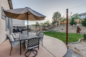 A patio with a table and chairs, a large umbrella, and a fenced yard with a statue. - 3BR 2BA, MTN view, relaxing yard (Reno)