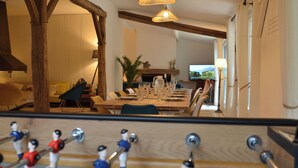 A dining area with a long table set for a meal, wooden beams on the ceiling, and a television on the wall.