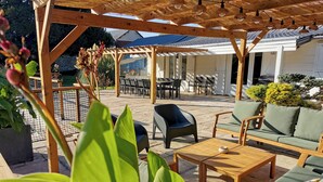 A wooden pergola with string lights, outdoor seating with cushions, and potted plants.