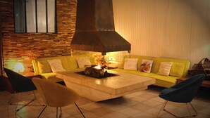 A living room with a yellow sofa, two armchairs, a fireplace, and a brick wall.