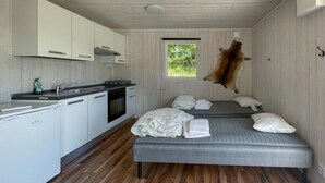 A compact room with a kitchenette, a bed with pillows, a window with a view of greenery, and a mounted animal hide on the wall. - Cozy home in Laholm with WiFi (Laholm)