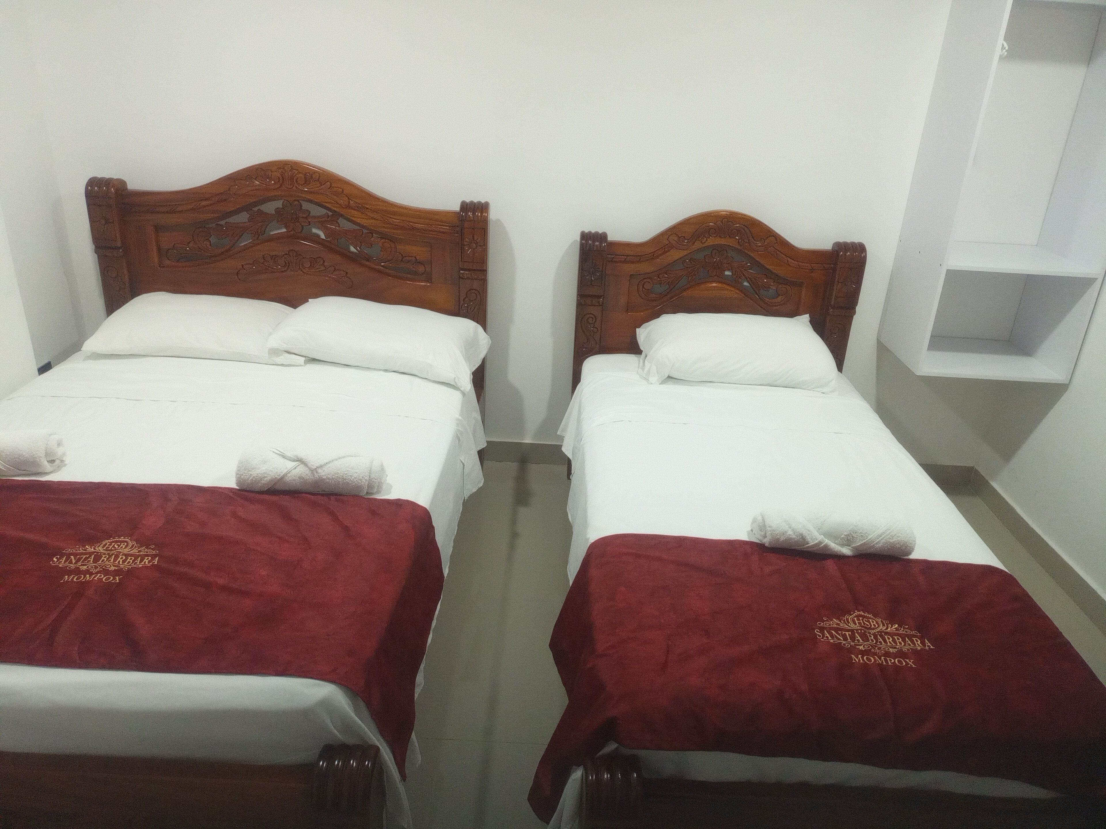 Dos camas individuales con cabeceros de madera, ropa blanca de cama y colchas rojas con texto bordado.