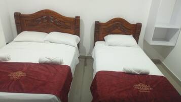 Dos camas individuales con cabeceros de madera, ropa blanca de cama y colchas rojas con texto bordado.