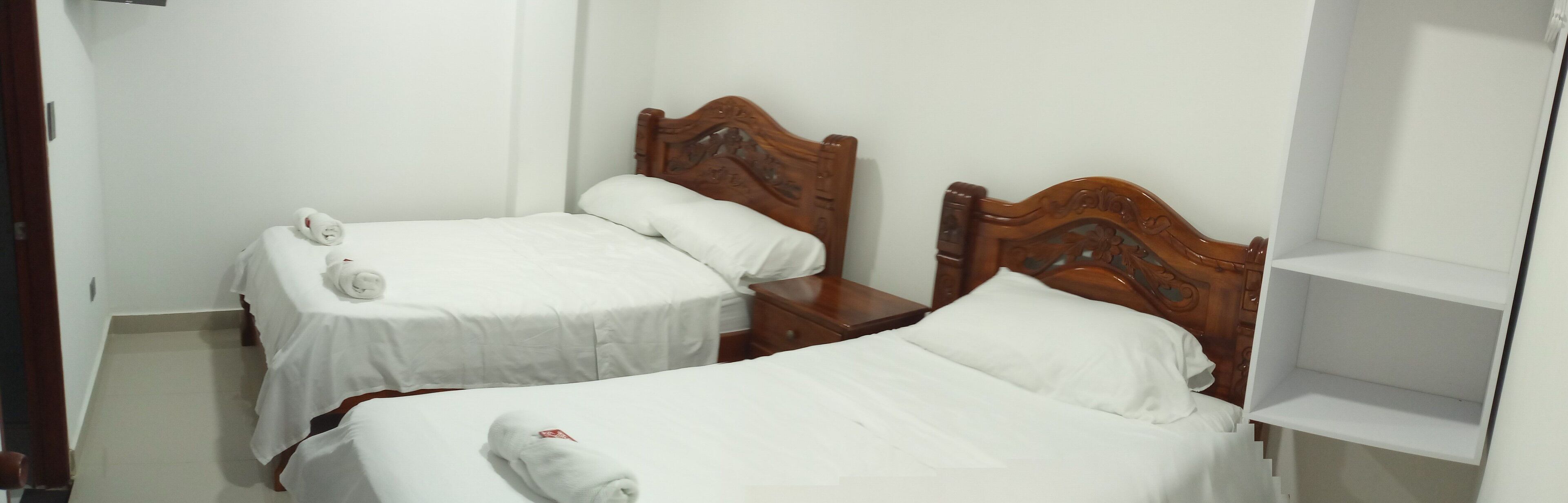 Two single beds with wooden headboards, white bedding, and rolled towels.