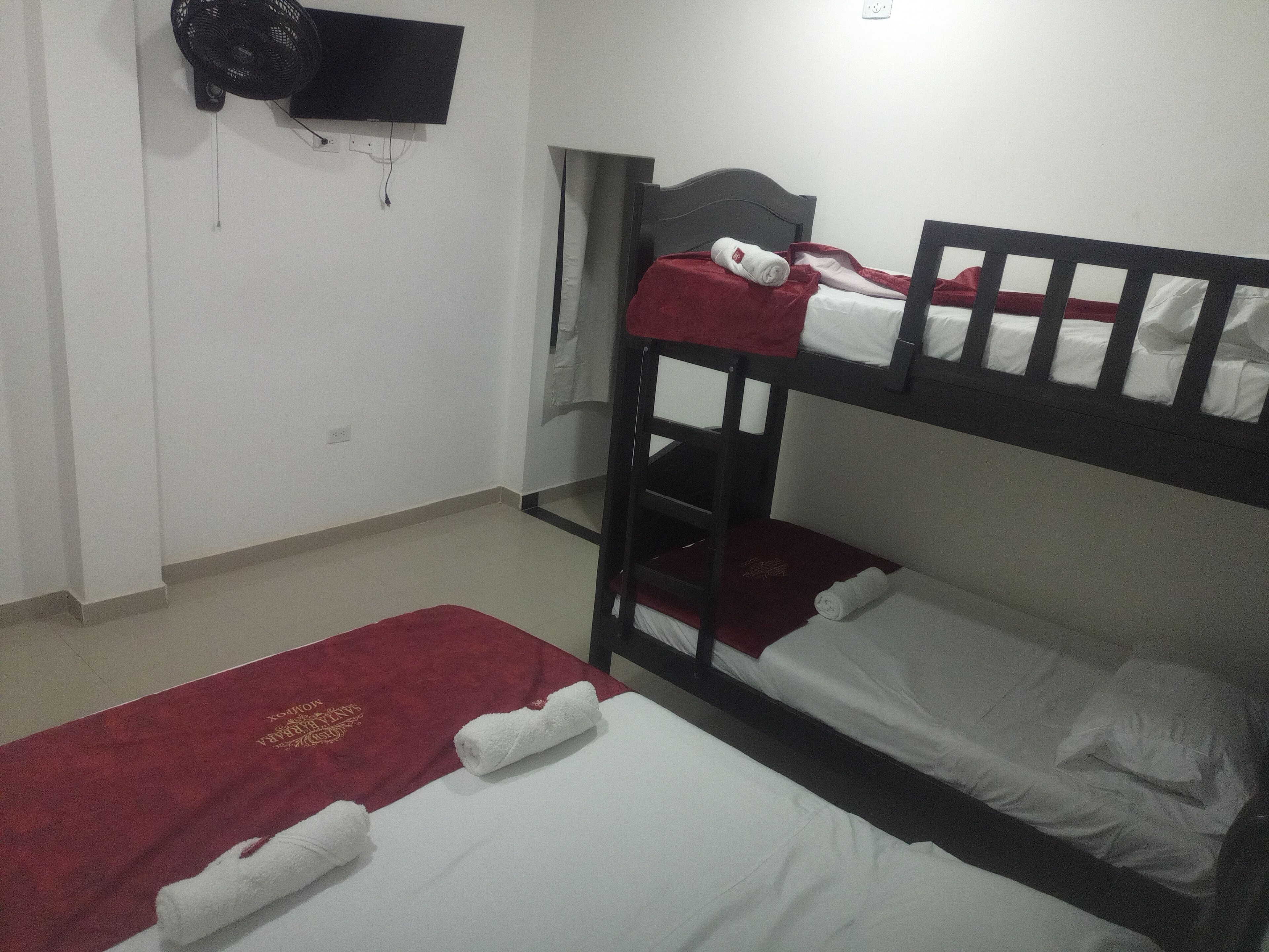Quarto com duas beliches, uma televisão presa à parede e uma toalha vermelha no chão.