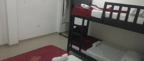 A room with two bunk beds, a TV mounted on the wall, and a red towel on the floor.