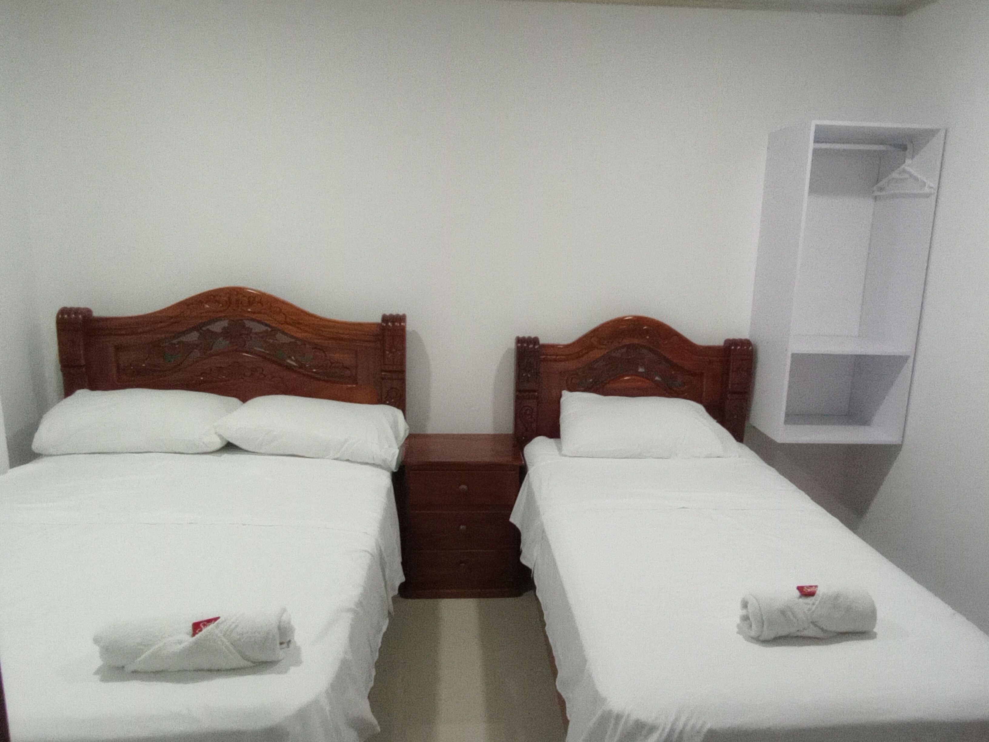 A room with two wooden beds, each with white linens and towels. There is a small wooden nightstand between the beds.