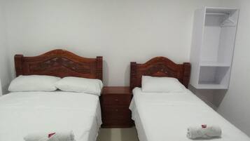 A room with two wooden beds, each with white linens and towels. There is a small wooden nightstand between the beds.