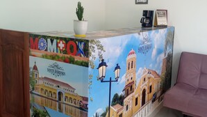 A reception desk with a colorful mural, a potted plant, framed certificates, and a coffee machine. - Hotel Santa Bárbara Mompox  (Mompos)