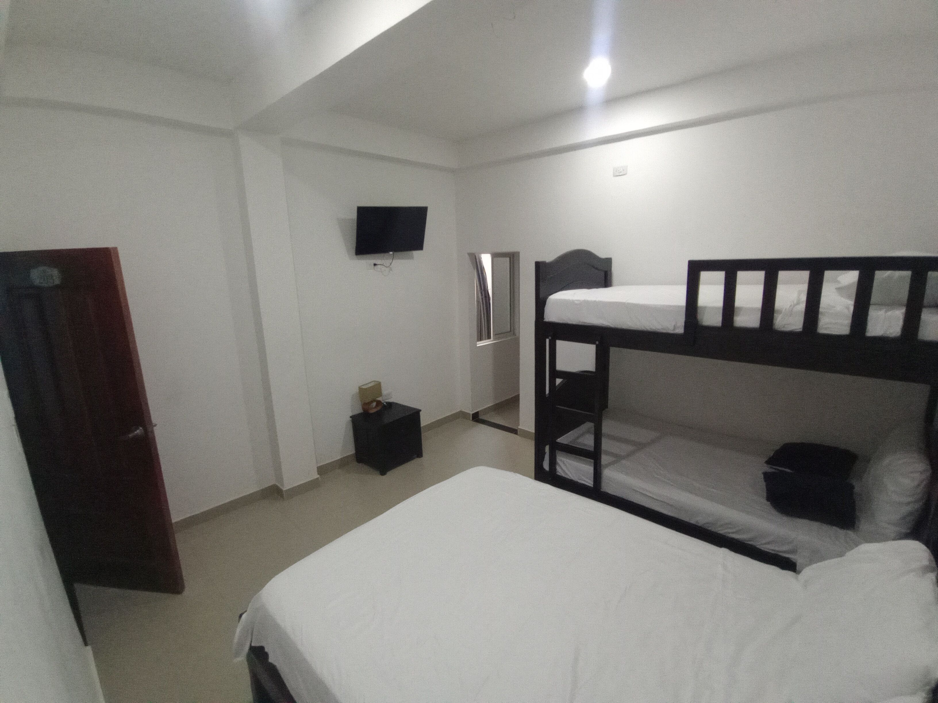 A room with bunk beds, a television mounted on the wall, a small bedside table, and a door.