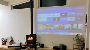 Una sala de estar con chimenea, un sofá, un perro y un proyector de pared que muestra servicios de transmisión.