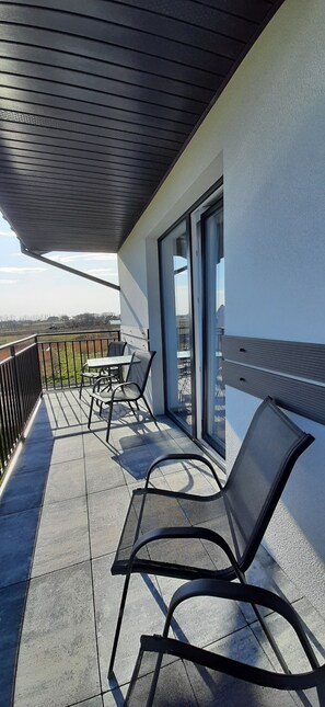 A balcony with a table and chairs, a view of the countryside, and a building with a modern design. - Apartamenty Jasieńczyk (Mielenko)