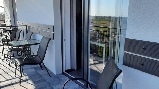 A modern outdoor seating area with a glass door leading to a balcony, featuring a tiled floor and contemporary metal chairs. - Apartamenty Jasieńczyk (Mielenko)