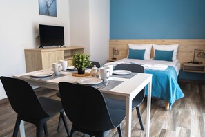 A modern hotel room with a neatly made bed, a dining area with a table set for two, and a television on a wooden cabinet. - Apartamenty Jasieńczyk (Mielenko)