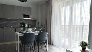 A modern kitchen with grey cabinets, a microwave, and a dining area with a table and chairs. - Apartamenty Jasieńczyk (Mielenko)