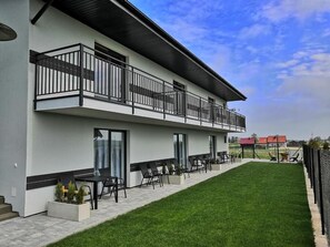 A modern building with a flat roof, a balcony with black railings, and a well-maintained lawn. - Apartamenty Jasieńczyk (Mielenko)