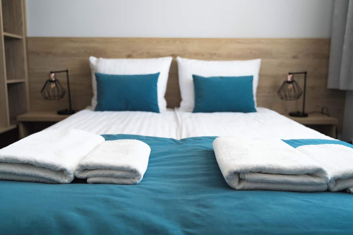 A double bed with white and teal bedding, two pillows, and two folded white towels.
