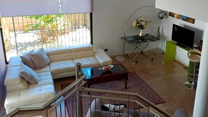 Un soggiorno moderno con divano, tavolino da caffè e televisione. Si vede una scala con ringhiera che conduce a un livello superiore.