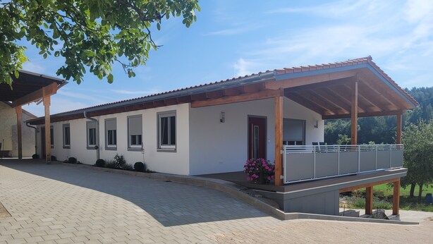 Ein modernes, zweistöckiges Haus mit überdachter Veranda und Balkon.