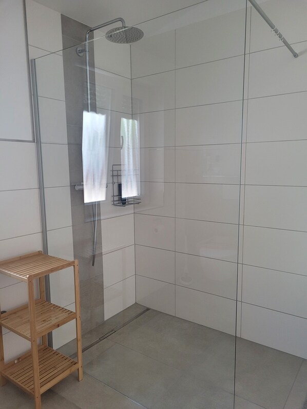 A shower with a glass door, a wooden shelf, and a tiled wall.