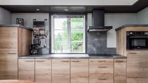 Une cuisine moderne avec des meubles en bois, une cuisinière noire et une fenêtre donnant sur un paysage verdoyant.