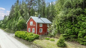 Une maison rouge avec un toit en métal, entourée d’une forêt verdoyante et dense.