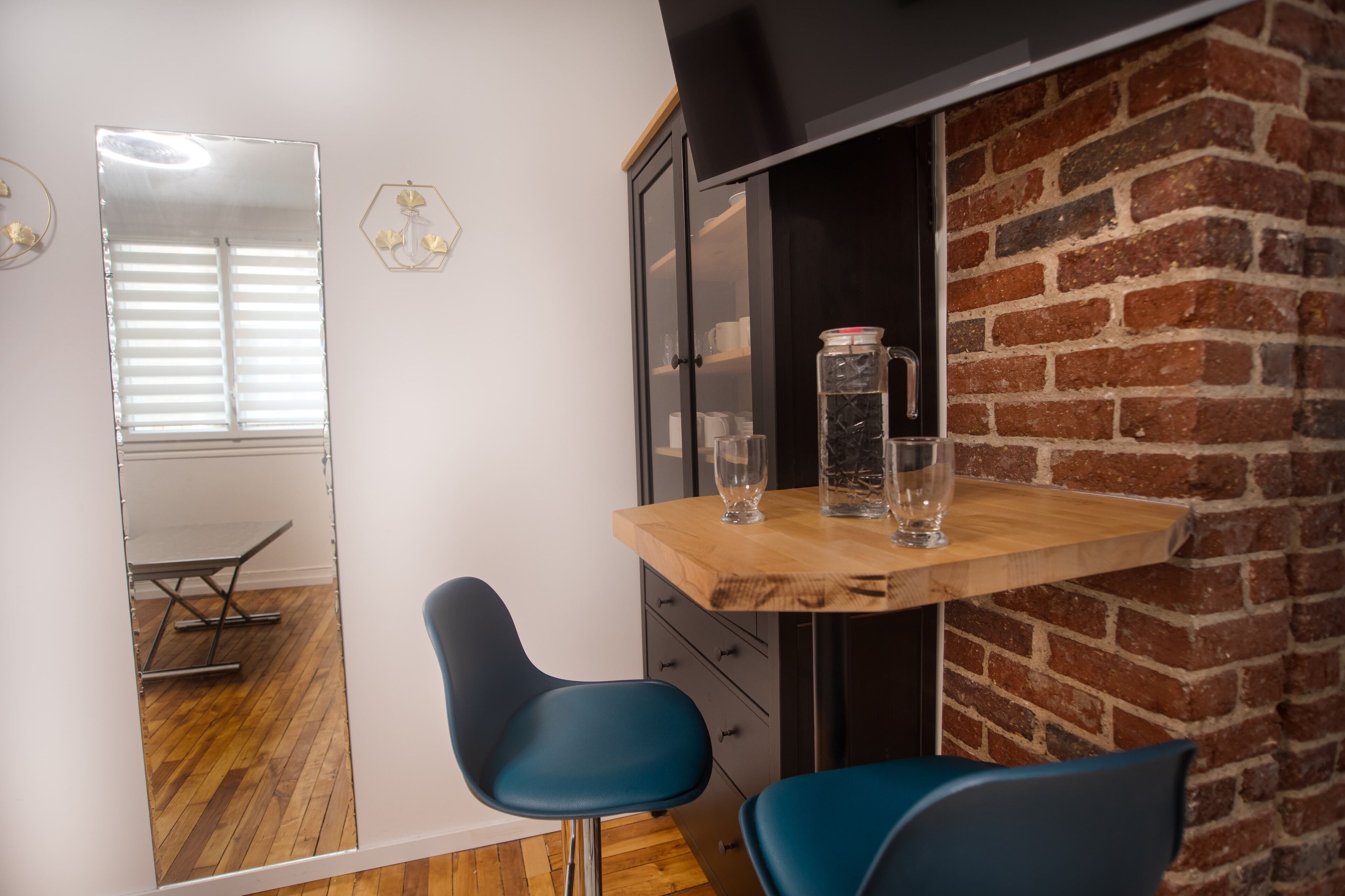 Una habitación con una mesa de madera, dos sillas azules, un armario negro y una pared de ladrillo.