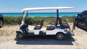 Un carrito de golf estacionado en una zona arenosa con vista despejada al océano y la playa al fondo.