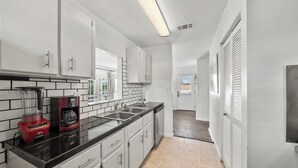 Una cocina moderna con armarios blancos, encimera negra y cafetera.