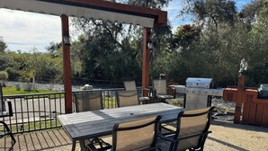 Une terrasse extérieure avec une table et des chaises, une pergola et un barbecue.