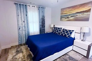 A bedroom with a bed, curtains, a nightstand, a lamp, and a painting on the wall.