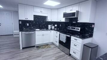 Una cocina moderna con armarios blancos, encimera negra y electrodomésticos de acero inoxidable.
