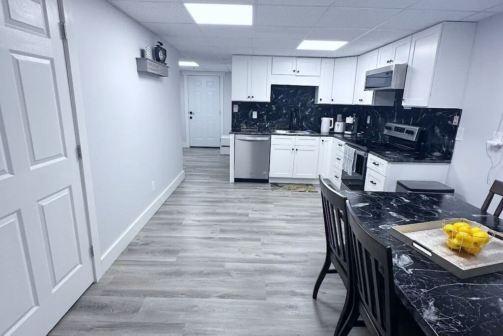 Una cocina con armarios blancos, una encimera negra y una zona de comedor con mesa y sillas.