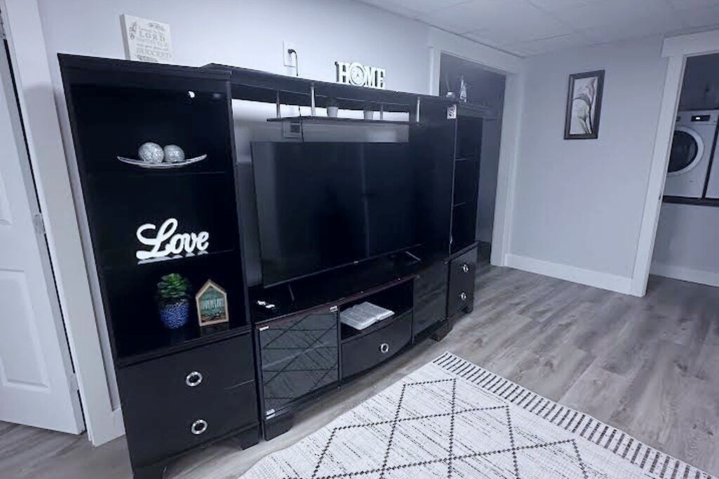 A modern living room with a large flat-screen TV, a black entertainment unit with a 'Love' sign, and a patterned rug.