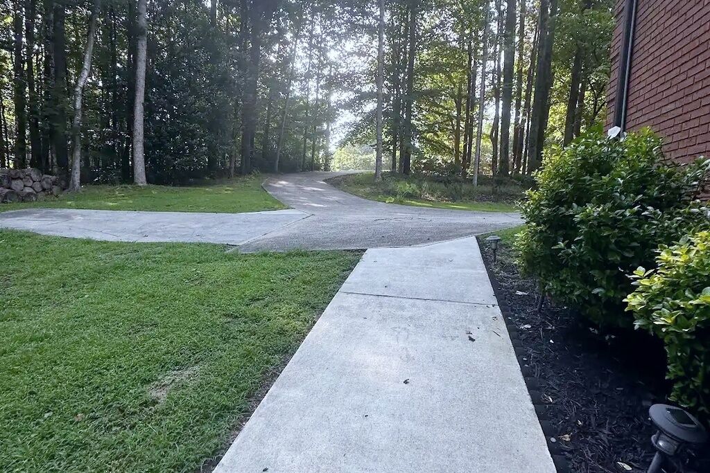A paved driveway leading to a building with a brick facade, surrounded by a grassy area and trees.