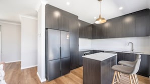 Een moderne keuken met donkere kastjes, een roestvrijstalen koelkast, een centraal eiland met een barkruk en een hanglamp.