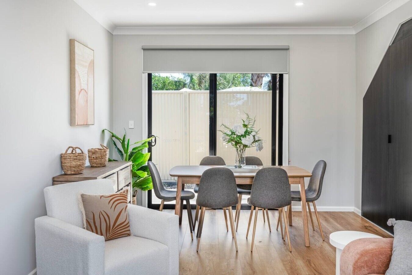 A modern dining area with a wooden table, grey chairs, and a large window with a view of greenery.