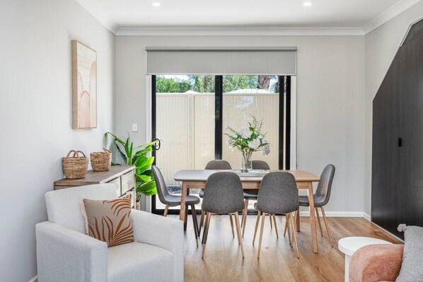 A modern dining area with a wooden table, grey chairs, and a large window with a view of greenery.