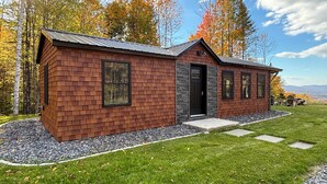 Una casa de ladrillo de dos pisos con puerta y ventanas negras, rodeada de un césped cuidado y árboles.
