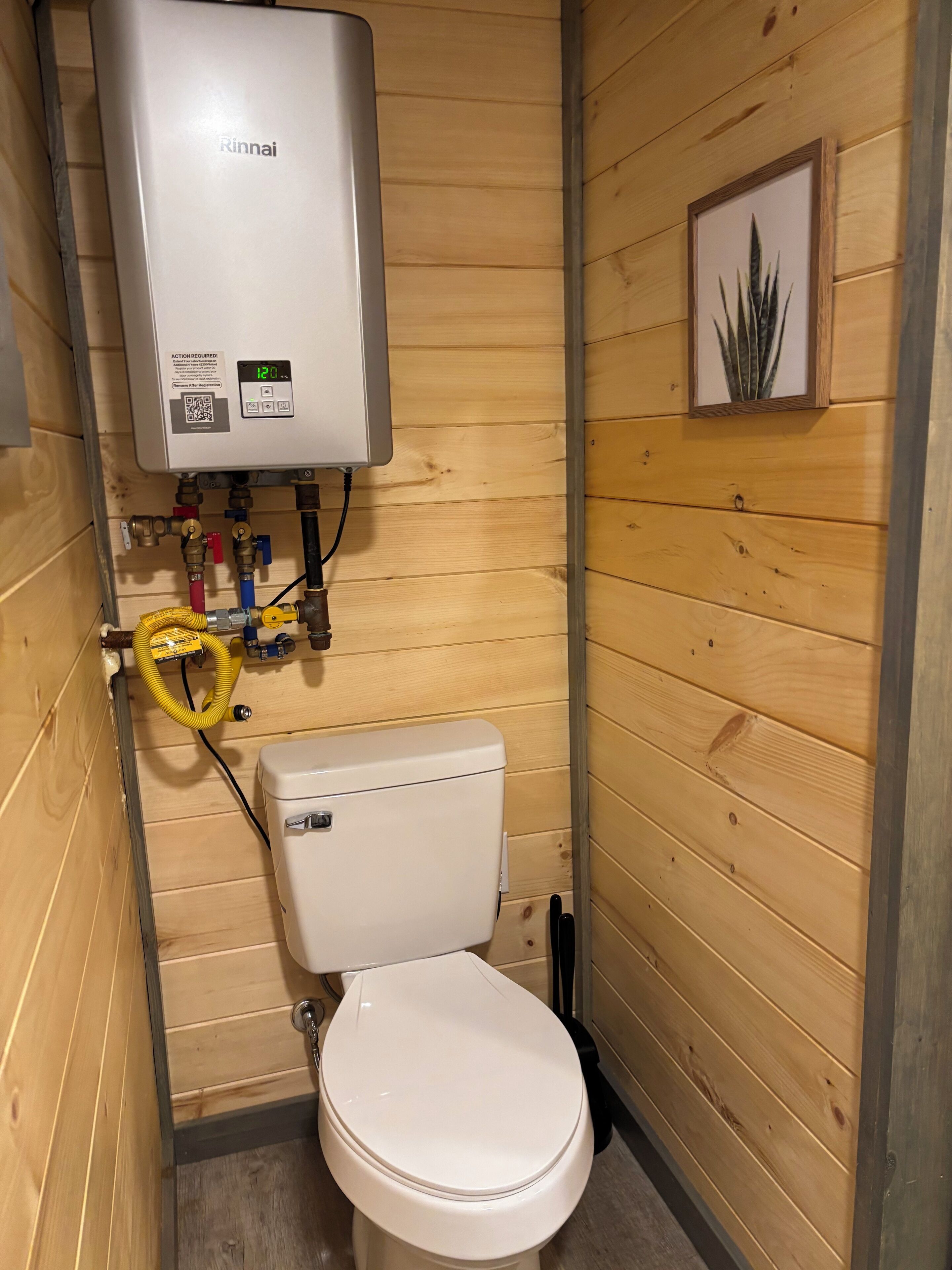 Un bagno con un water bianco, uno scaldacqua Rinnai e pareti in legno.