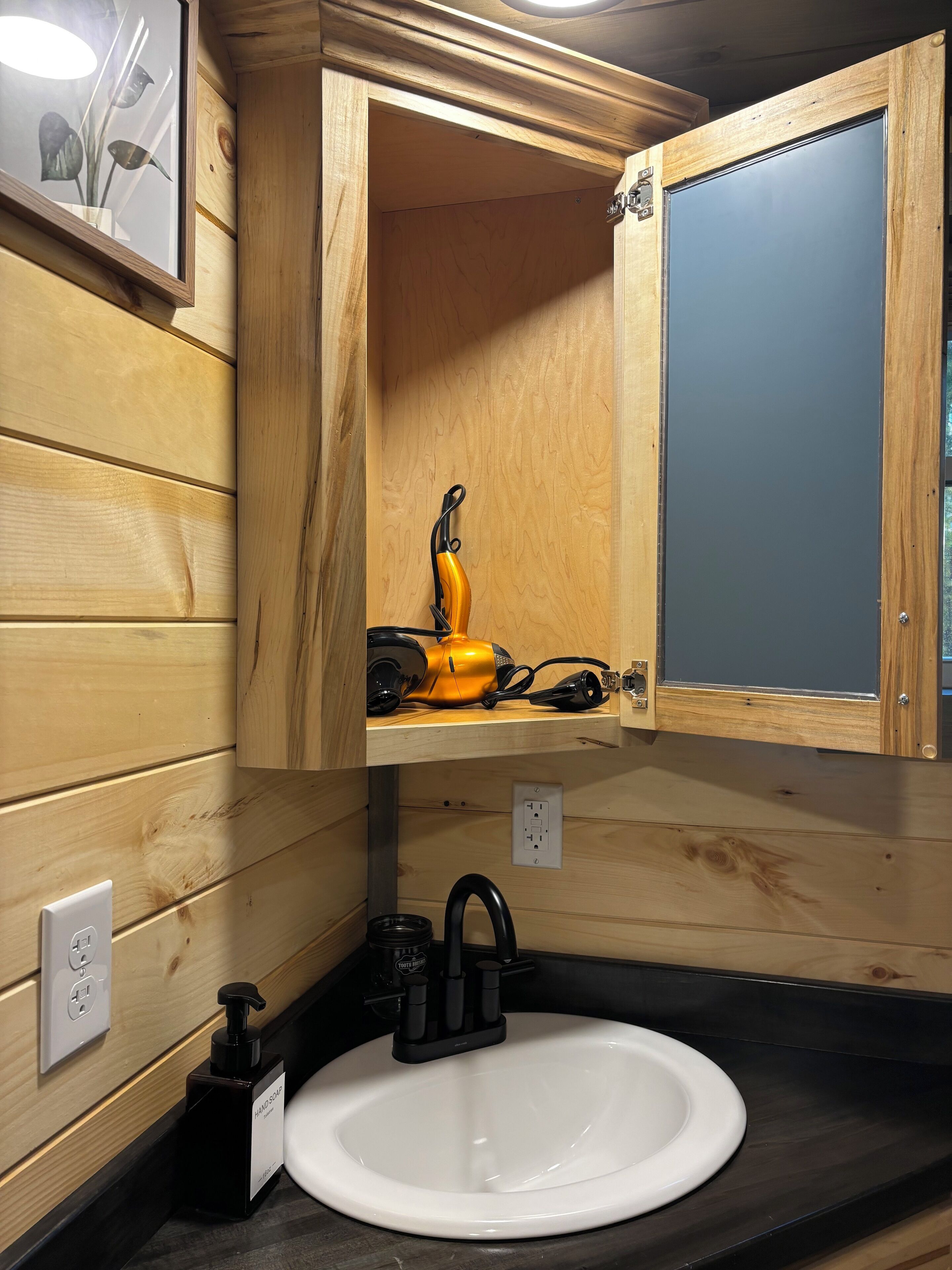 Un baño de madera con un lavabo blanco, un espejo y un cepillo de dientes eléctrico amarillo sobre una repisa.