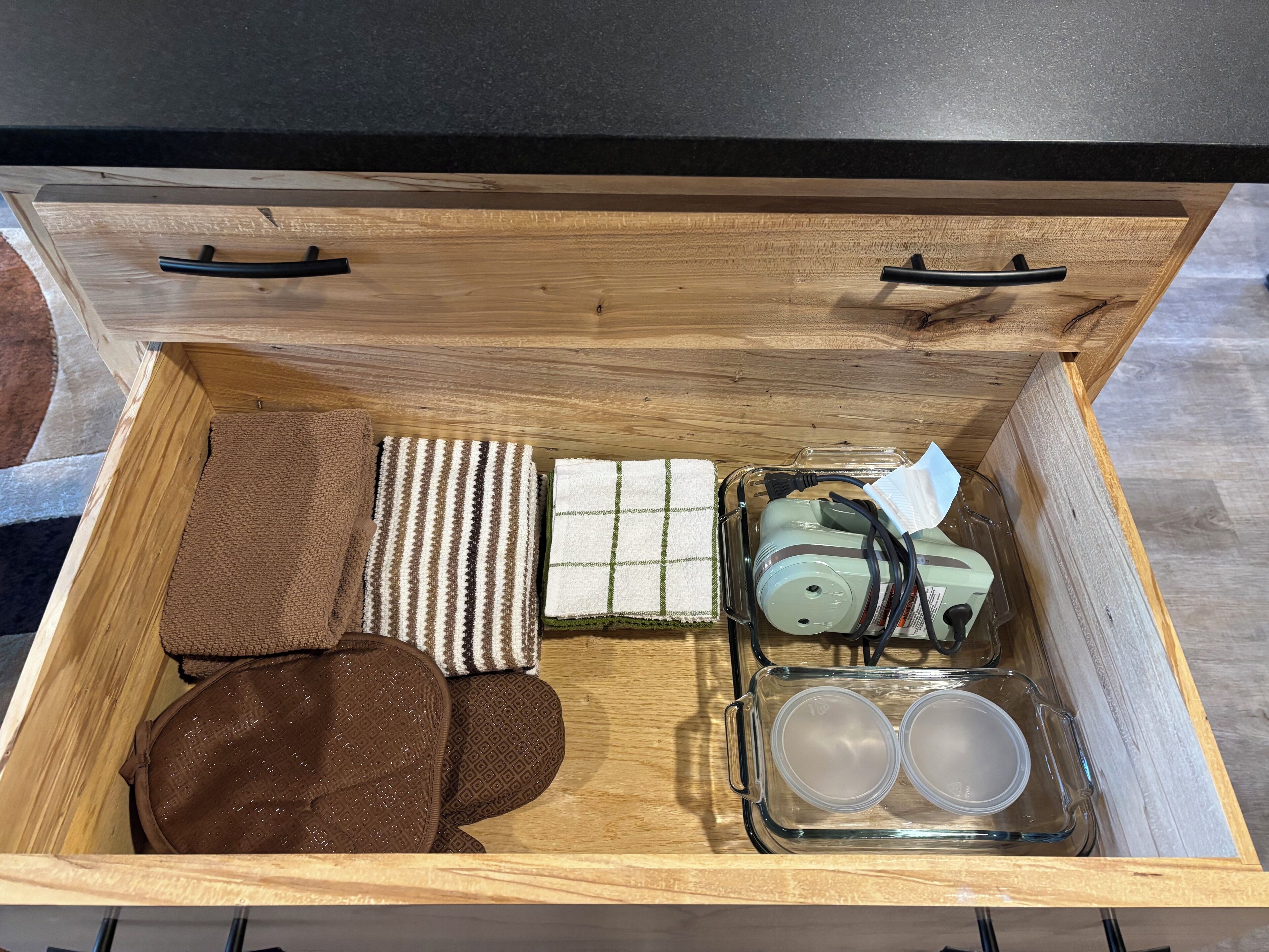 Een houten lade met vakken, gevuld met een gestreepte handdoek, een bruine tas, een groene fles en twee transparante bakjes.