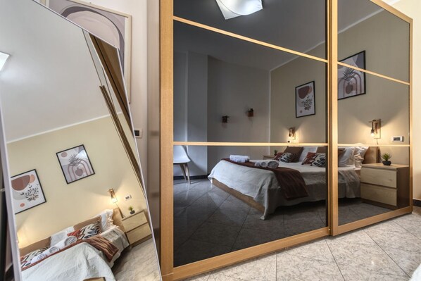 A modern bedroom with a large mirror, a bed with multiple pillows, a nightstand, and wall art.
