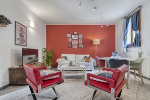 A living room with a white sofa, red armchairs, a coffee table, and a dining area with a table and chairs.